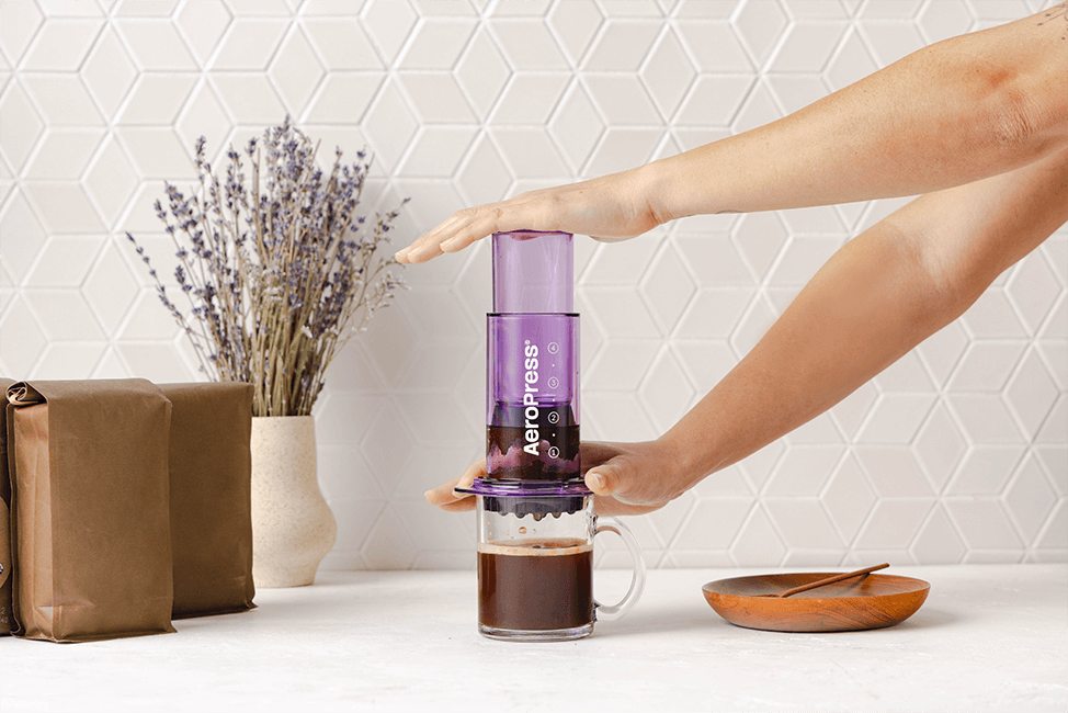 Person pressing coffee through AeroPress Clear Purple into a clear mug in a kitchen