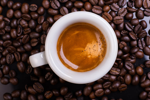 Small cup of espresso on top of coffee beans