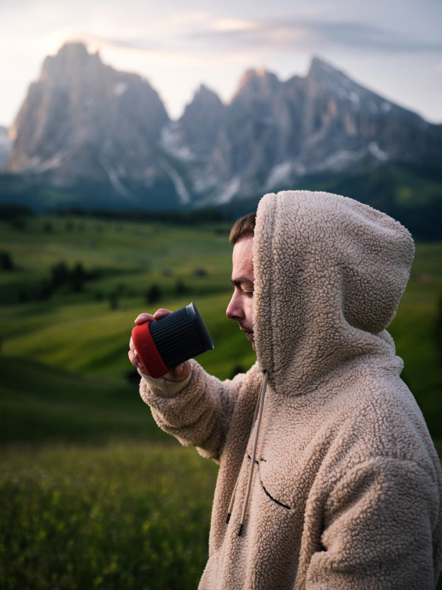 Man drinking from AeroPress Go travel cup next to mountains