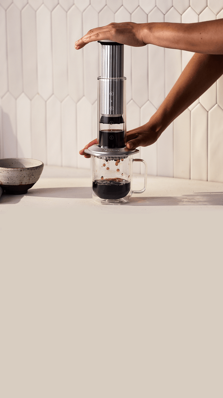Person using an AeroPress Premium coffee maker on a kitchen counter.