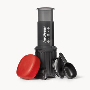 AeroPress Go coffee maker with red lid and black scoop on a white background
