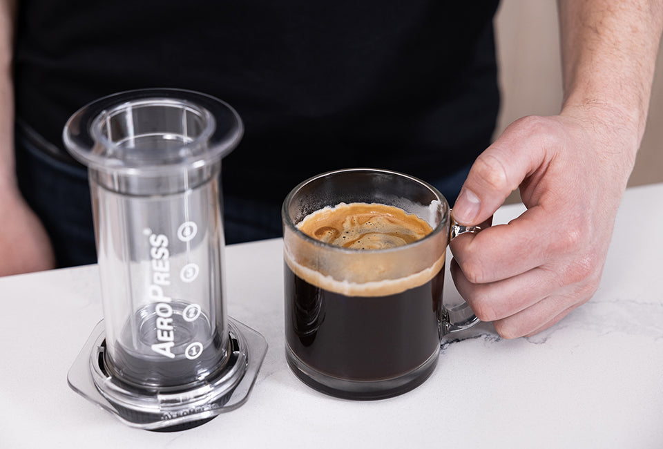 AeroPress Clear coffee maker next to mug with crema