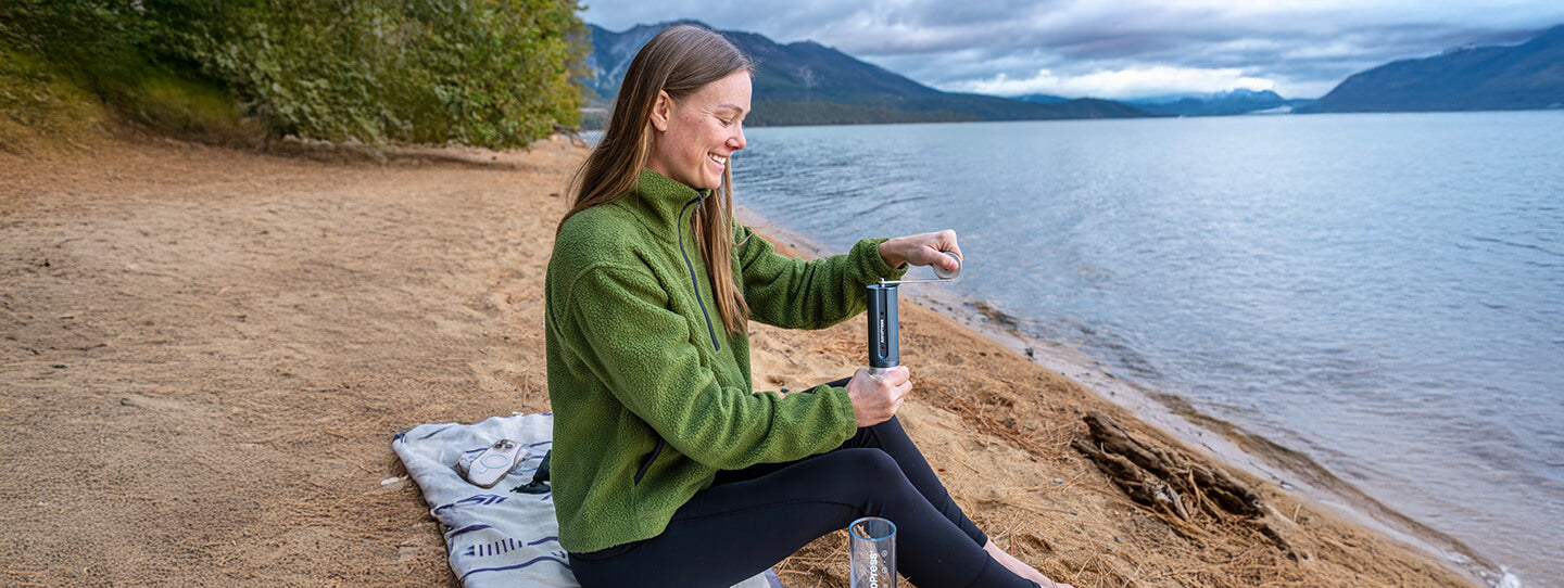 Woman using coffee grinder on a beach