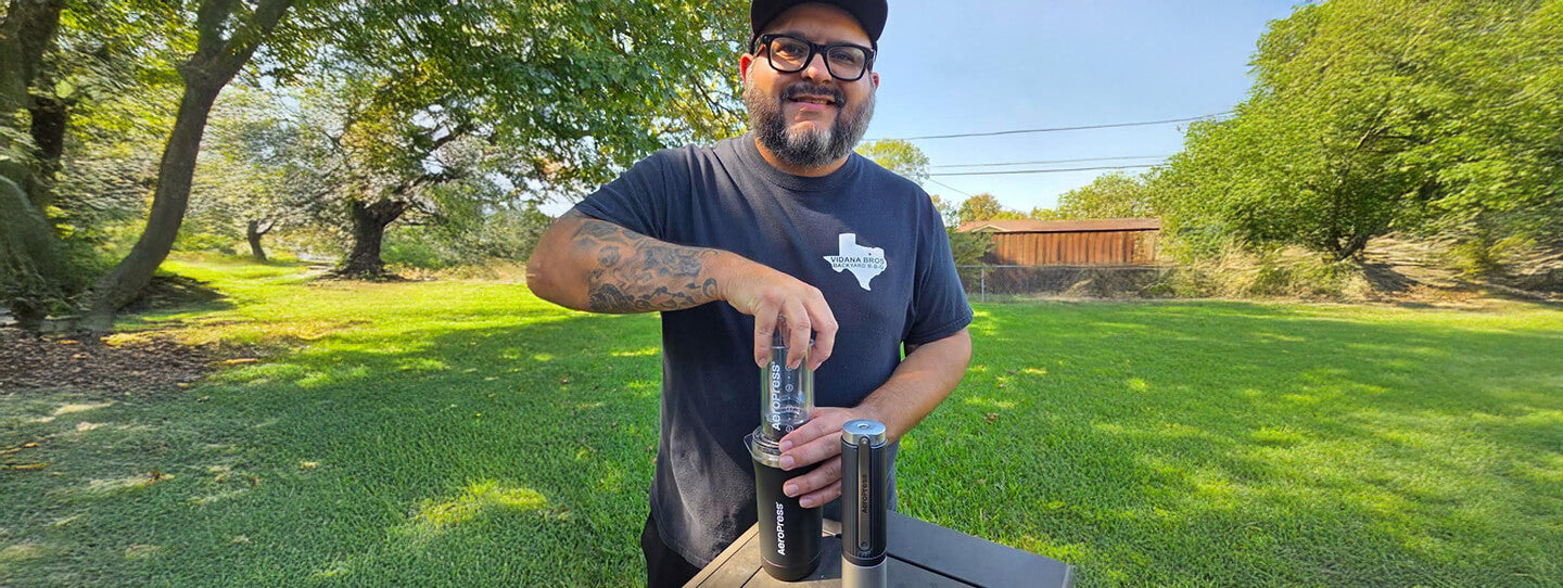 Person brewing with an AeroPress coffee maker outdoors