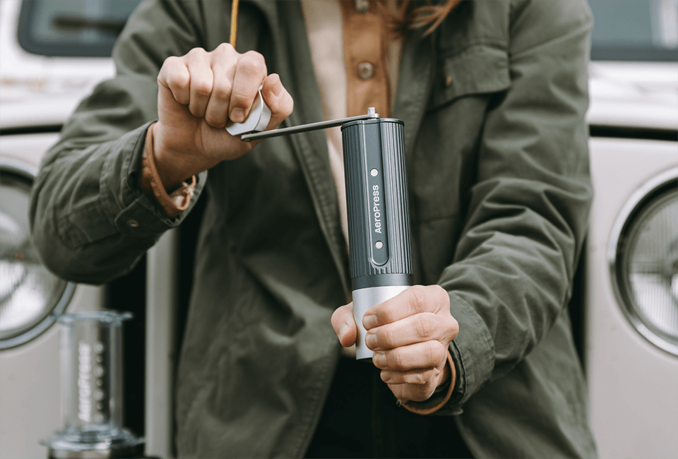 Person using the AeroPress Manual Grinder in front of a white Jeep