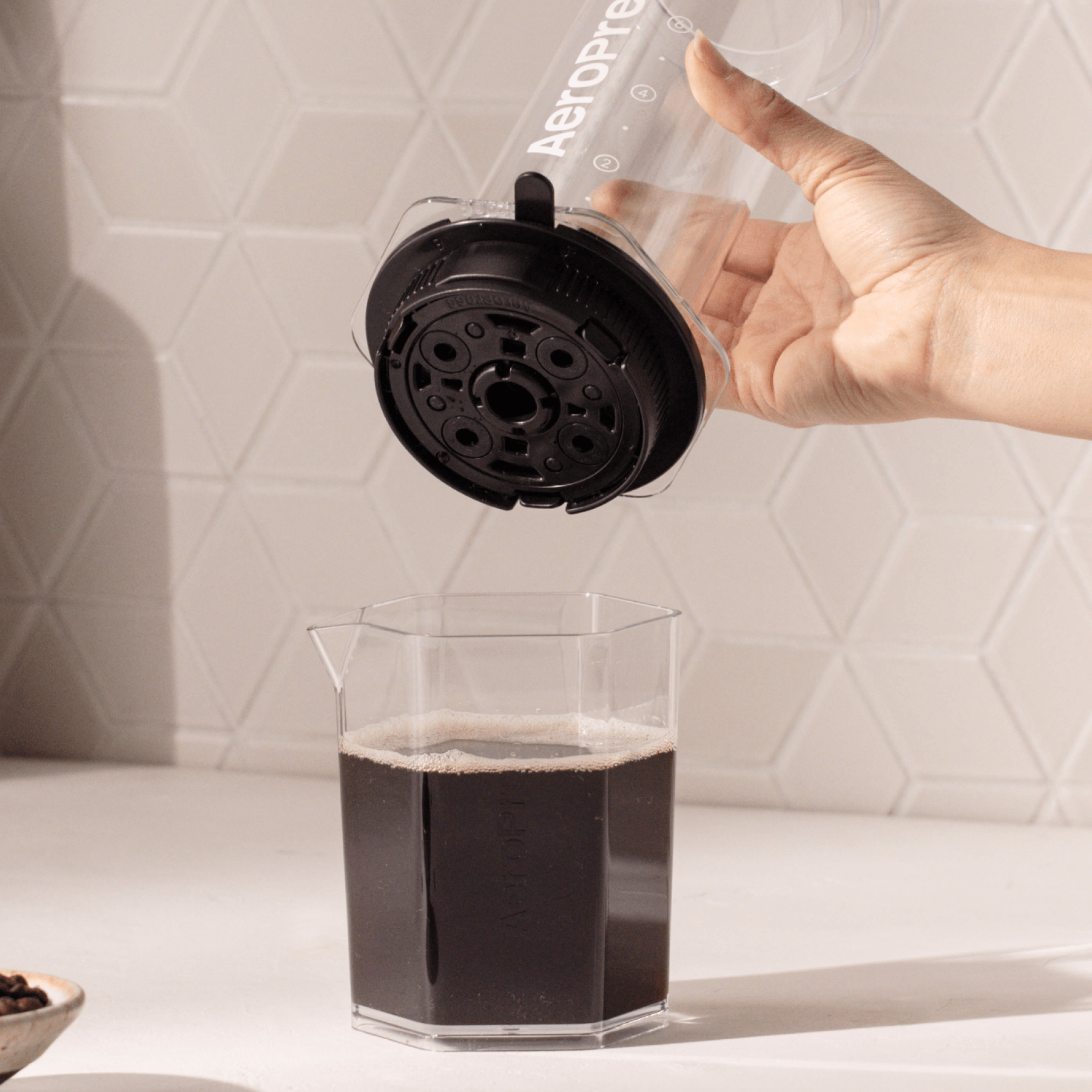 Person using an AeroPress to make coffee on a white countertop.