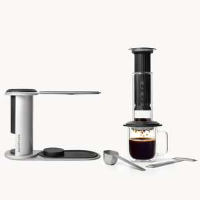 AeroPress Premium Black coffee maker with a glass mug of coffee on a white background #color_black