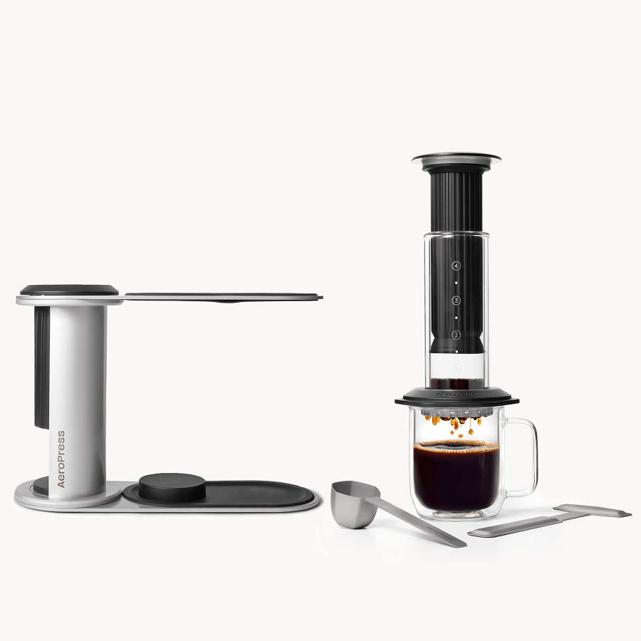 AeroPress Premium Black coffee maker with a glass mug of coffee on a white background #color_black