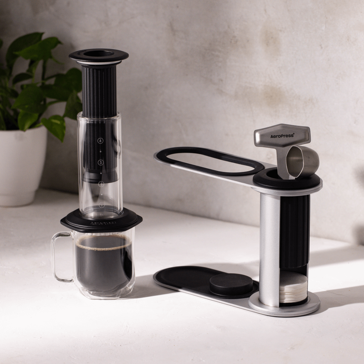 AeroPress Premium coffee maker on a white surface with a plant in the background #color_black