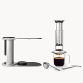 AeroPress coffee maker with a glass of coffee on a white background #color_silver