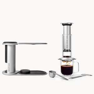 AeroPress coffee maker with a glass of coffee on a white background 