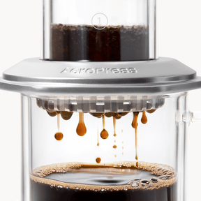 AeroPress Premium coffee maker with coffee being pressed through, showing the brewing process. #color_silver