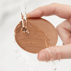 A person holding an AeroPress Gold Tone Filter under running water.