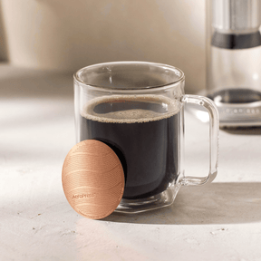 Clear glass mug with coffee inside and AeroPress Gold Tone Filter leaning against it