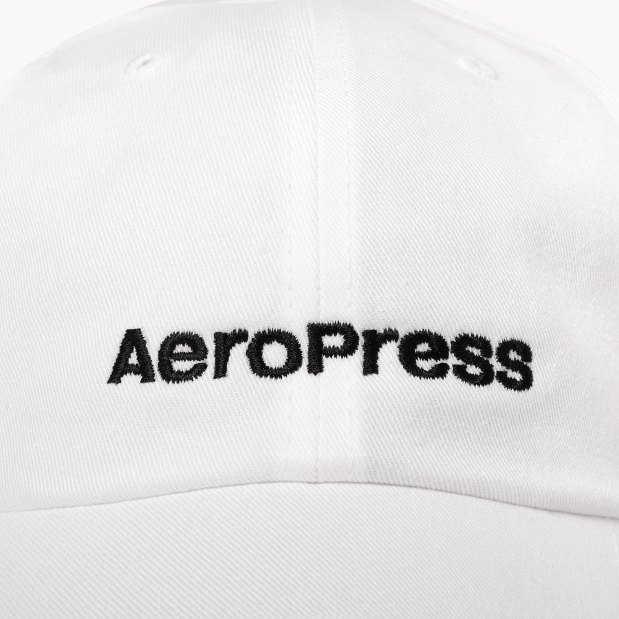Up close shot of a white cap with AeroPress logo on a white background #color_white