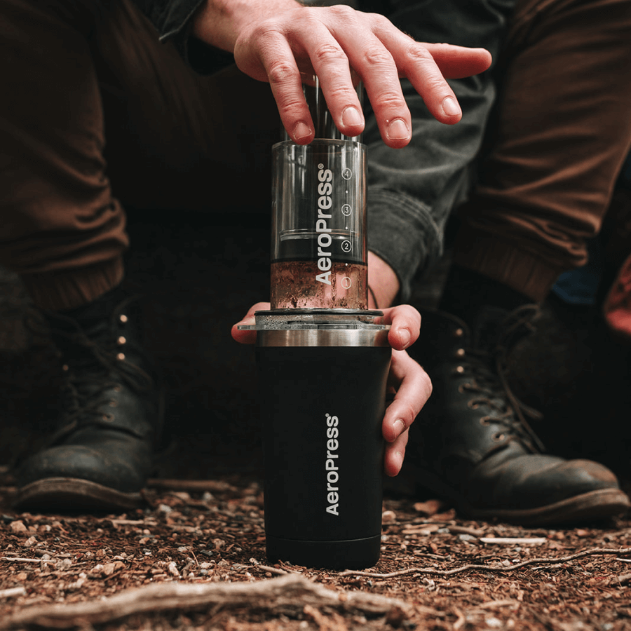 Person using an AeroPress outdoors on a natural background