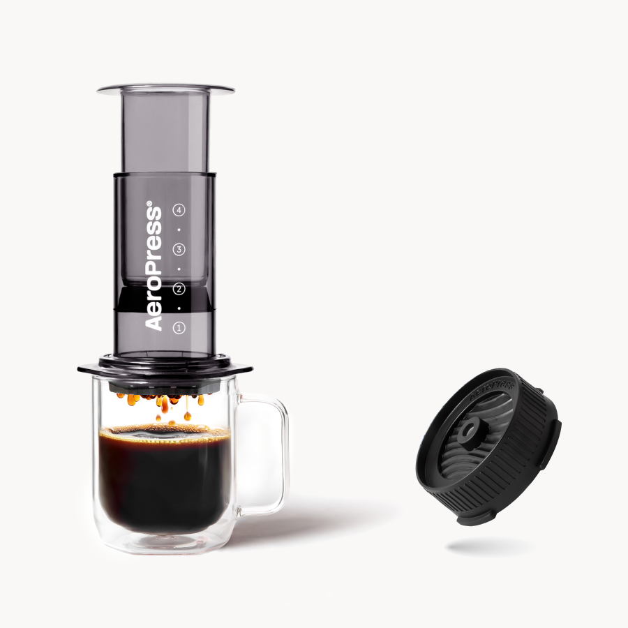 AeroPress Clear Black on glass mug next to Flow Control Cap on white background #color_black