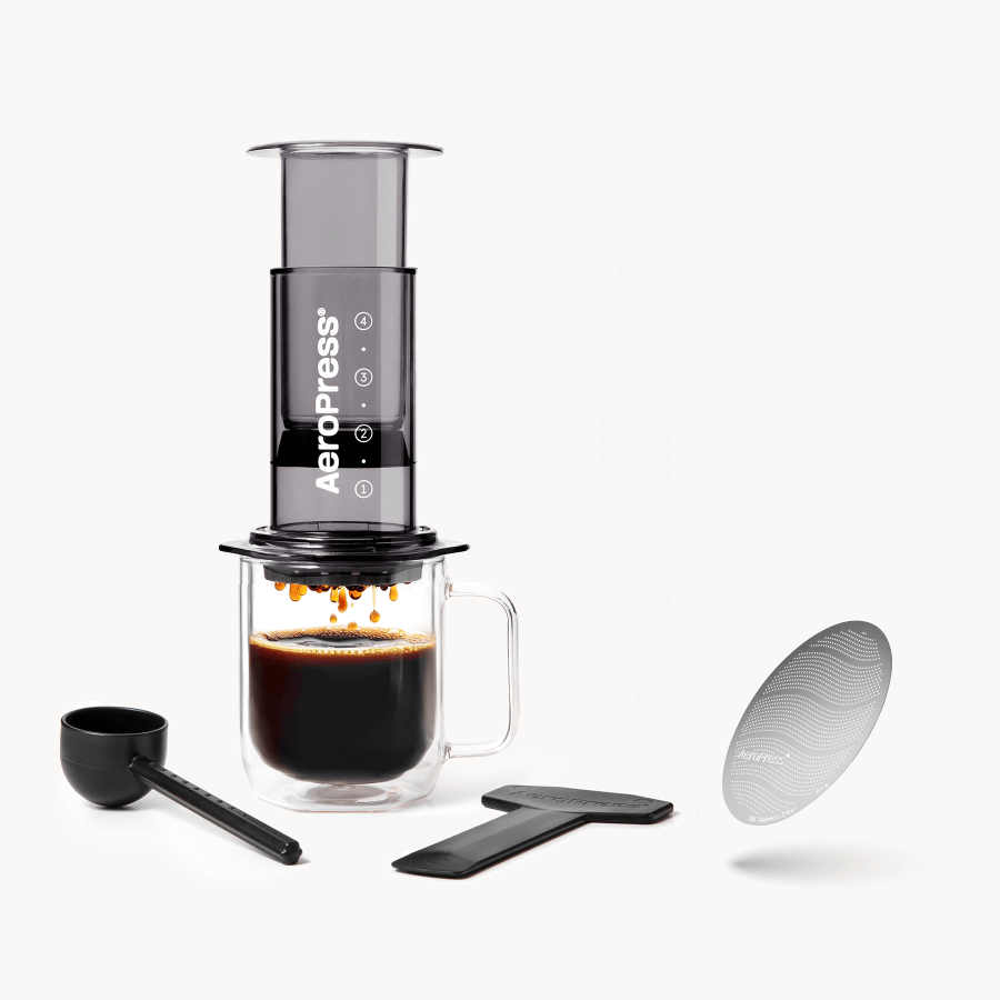 AeroPress coffee maker with a glass of brewed coffee and additional components on a white background #color_black