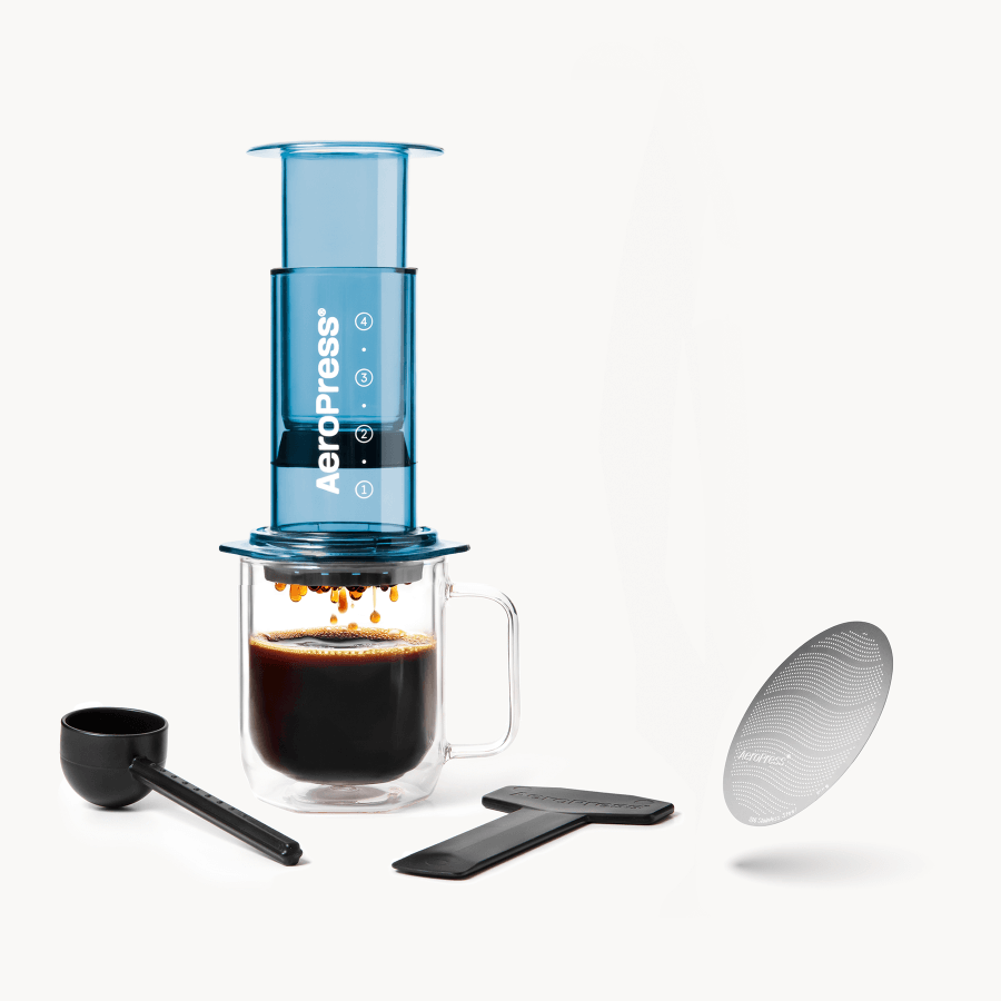 Blue AeroPress coffee maker with a glass mug, scoop, and filter on a white background #color_blue