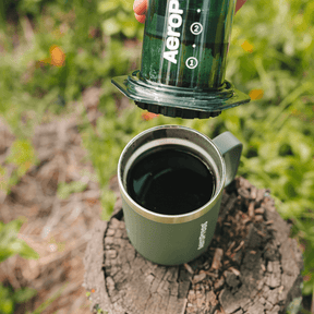 A person using an Aeropress to make coffee outdoors on a natural  background #color_green