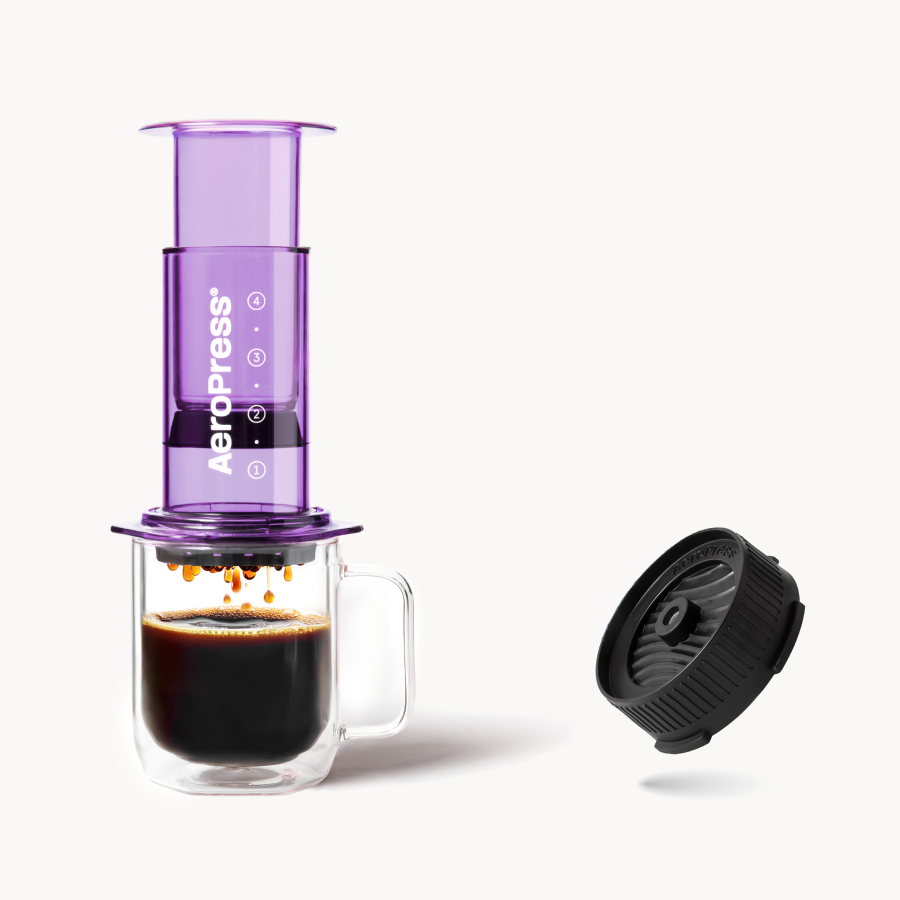 Purple AeroPress coffee maker with a glass mug of coffee and Flow Control Cap on a white background #color_purple