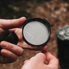 Person holding a coffee filter with a brand name against a blurred natural background  #color_purple