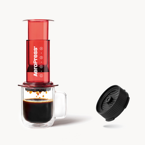 AeroPress Clear Red coffee maker with a cup of coffee and a black Flow Control Cap on a white background #color_red