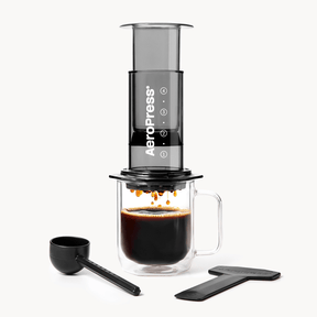 AeroPress  Clear Black coffee maker with a glass of brewed coffee and scoop on a white background #color_black