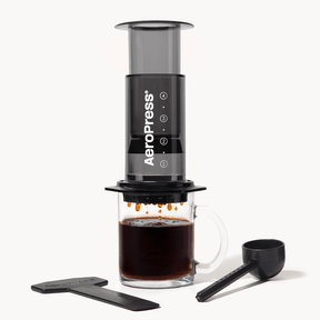 AeroPress  Clear Black coffee maker with a glass of brewed coffee and scoop on a white background #color_black