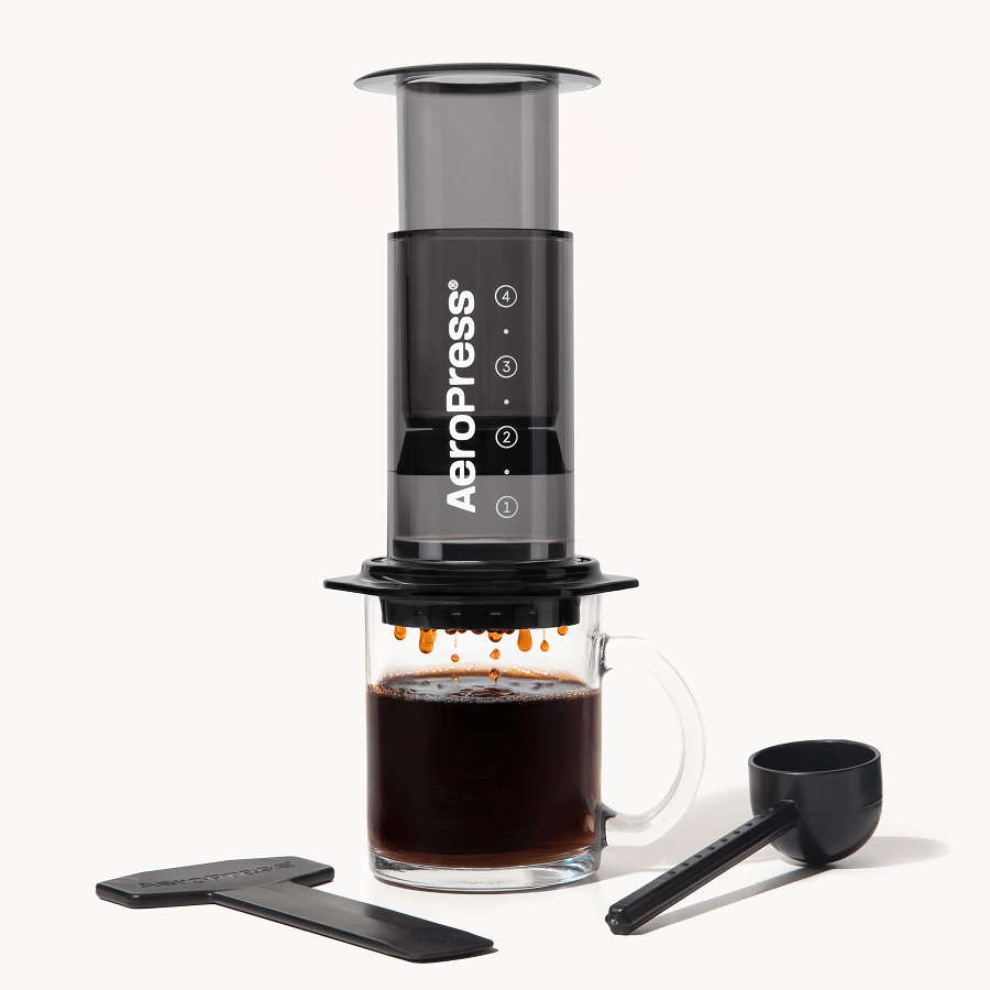 AeroPress  Clear Black coffee maker with a glass of brewed coffee and scoop on a white background #color_black