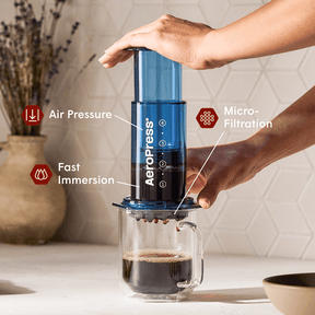 A person using an AeroPress coffee maker with labeled features on a kitchen counter.  #color_blue