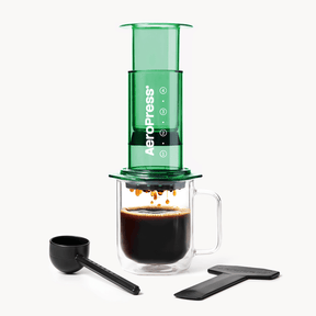 Green AeroPress coffee maker with a glass mug of coffee and scoop on a white background #color_green