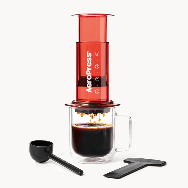 Aeropress Clear Red coffee maker with a glass of brewed coffee on a white background #color_red