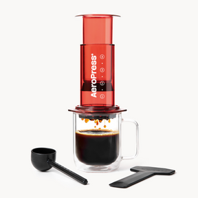 Aeropress Clear Red coffee maker with a glass of brewed coffee on a white background #color_red