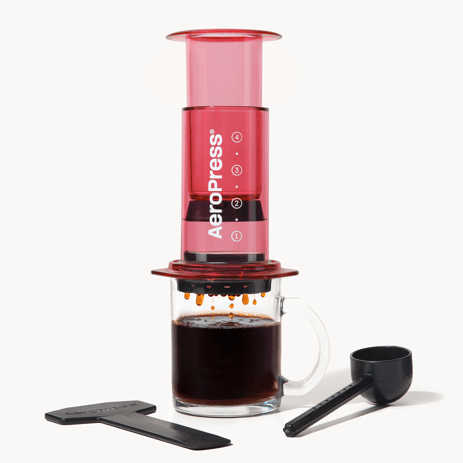 Aeropress Clear Red coffee maker with a glass of brewed coffee on a white background #color_red