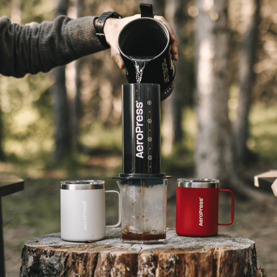 Person pouring coffee from an Aeropress into a mug outdoors.