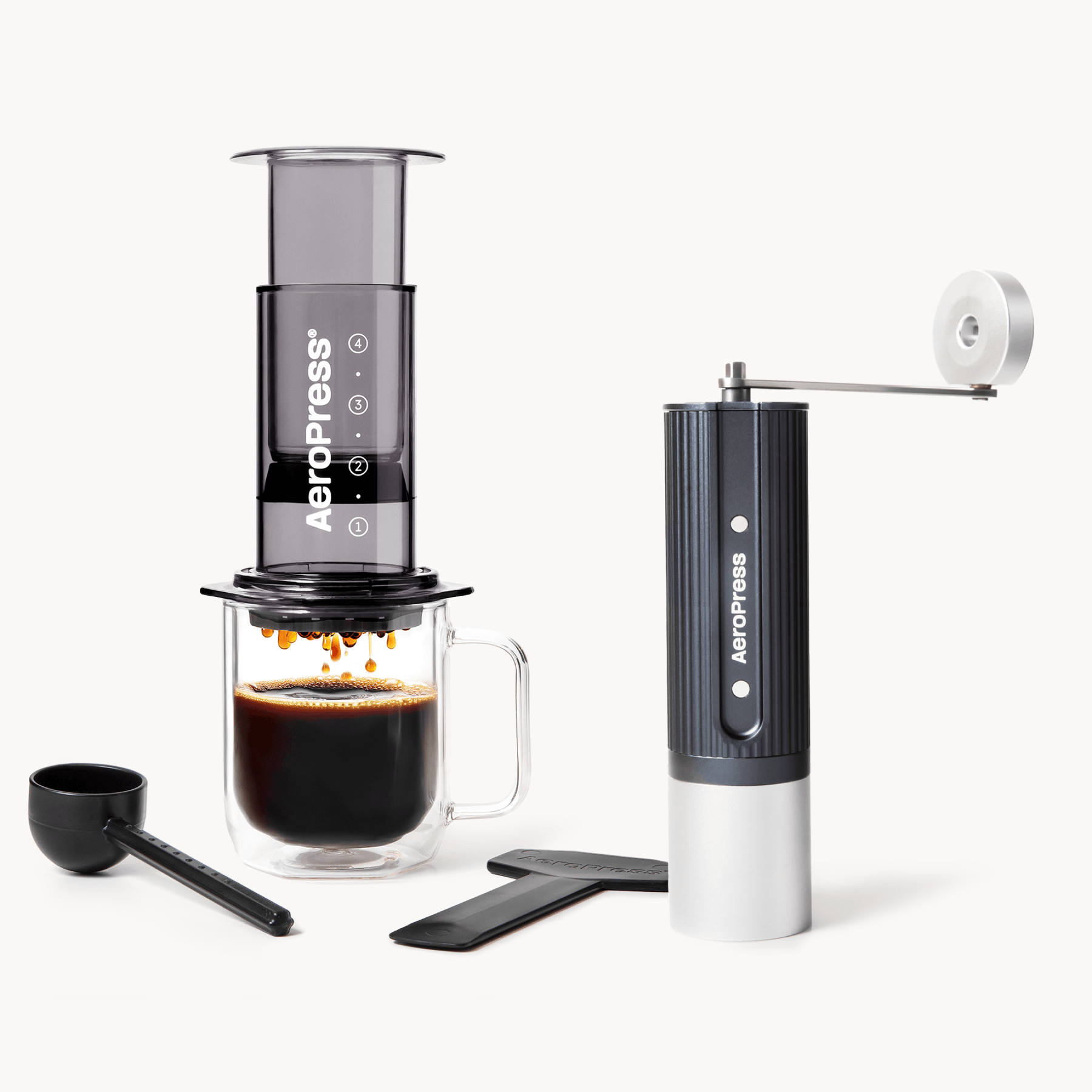 Aeropress coffee maker with a glass mug of coffee and a manual grinder on a white background #color_Black
