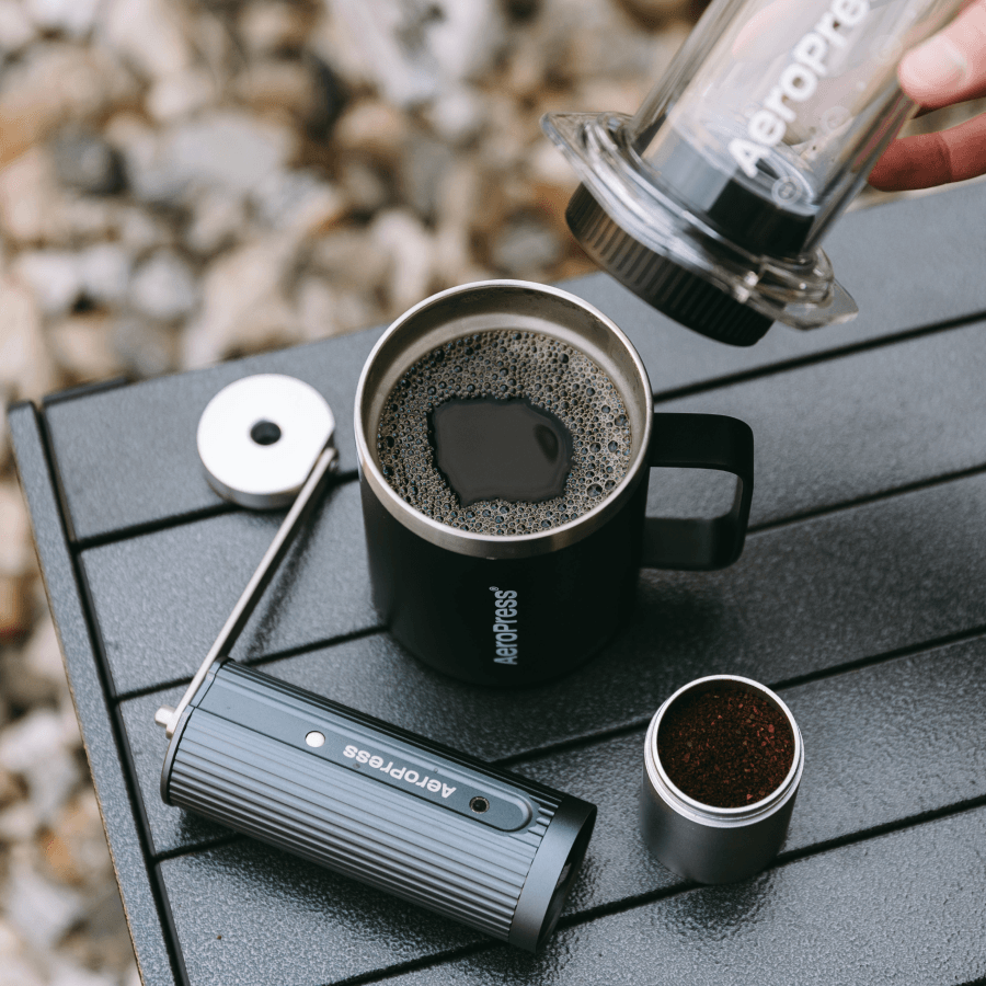 Aeropress coffee maker being used to pour coffee into a black mug on a wooden surface. #color_Black