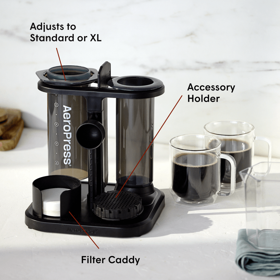 AeroPress coffee maker loaded into the Organizer Stand next to two mugs of coffee on a kitchen counter