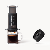 Aeropress coffee maker with a glass of brewed coffee on a white background