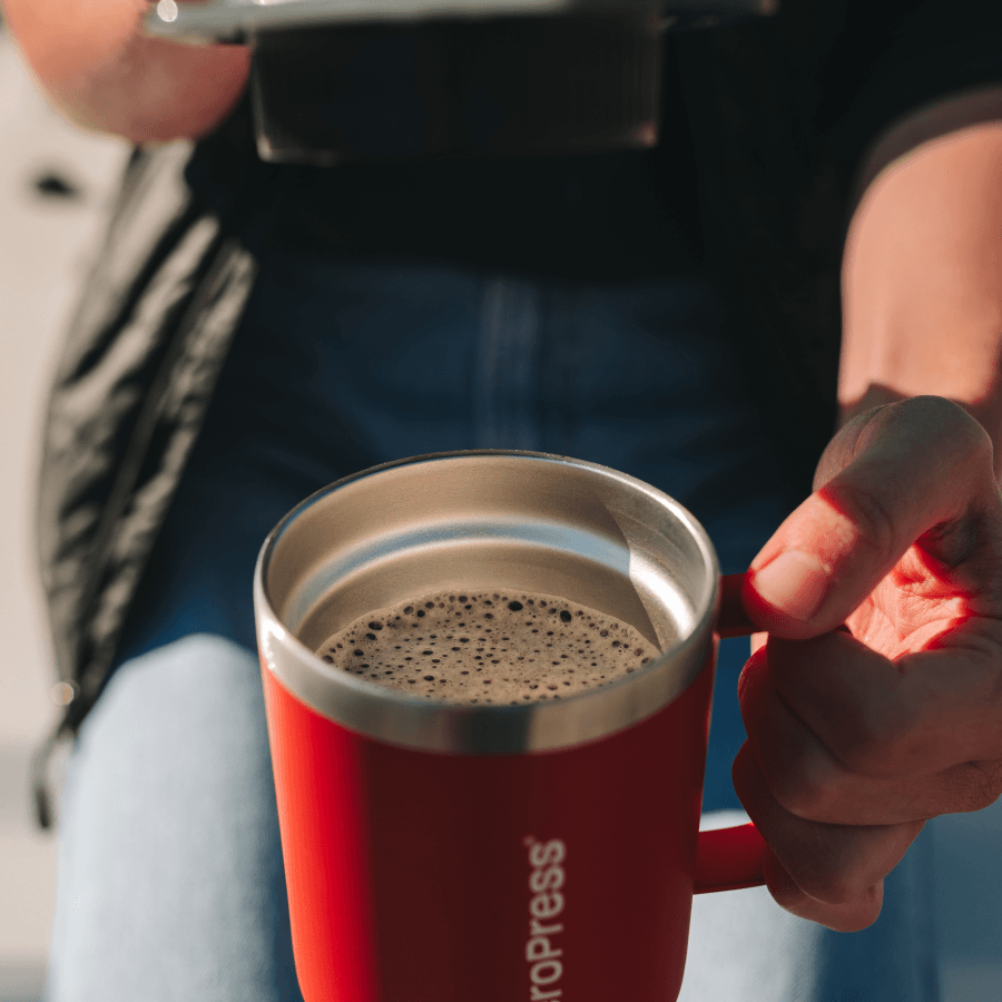 Person holding a red AeroPress stainless steel mug with coffee inside it