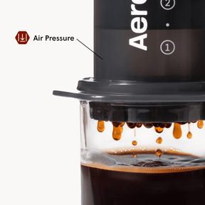 AeroPress Original coffee maker with coffee being pressed into a glass container, showing air pressure.