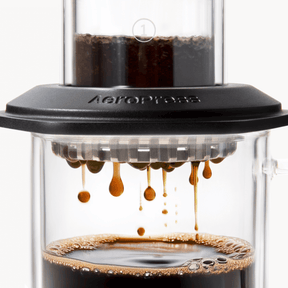 AeroPress Premium coffee maker with coffee being pressed through, showing the brewing process. #color_black