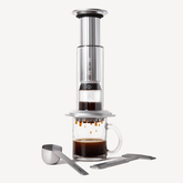 AeroPress Premium Coffee maker with a glass mug filled with coffee on a white background