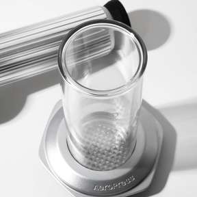 Clear glass AeroPress Premium chamber with metal base on a white  surface #color_silver