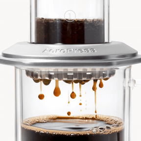 AeroPress Premium coffee maker with coffee being pressed through, showing the brewing process. #color_silver