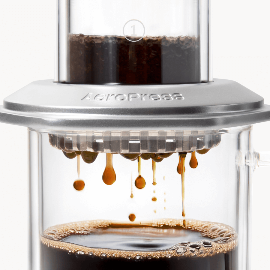 AeroPress Premium coffee maker with coffee being pressed through, showing the brewing process. #color_silver
