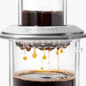 AeroPress Premium coffee maker with coffee being pressed through, showing the brewing process. #color_silver