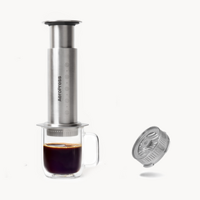 Aeropress Steel coffee maker with a glass of coffee and stainless steel flow control on a white background #color_silver
