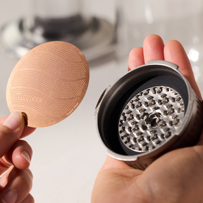 Person holding a steel flow control cap and a metal mesh filter. #color_silver